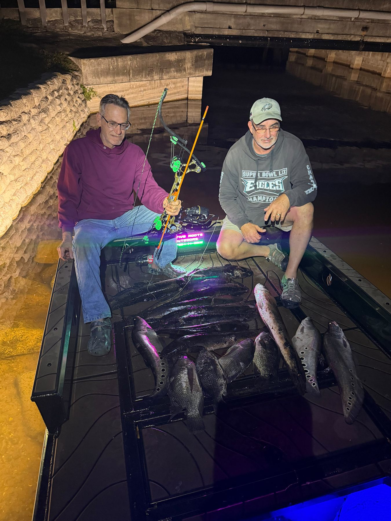 Two Native Roots guests sitting on the boat with a nighttime bowfishing catch