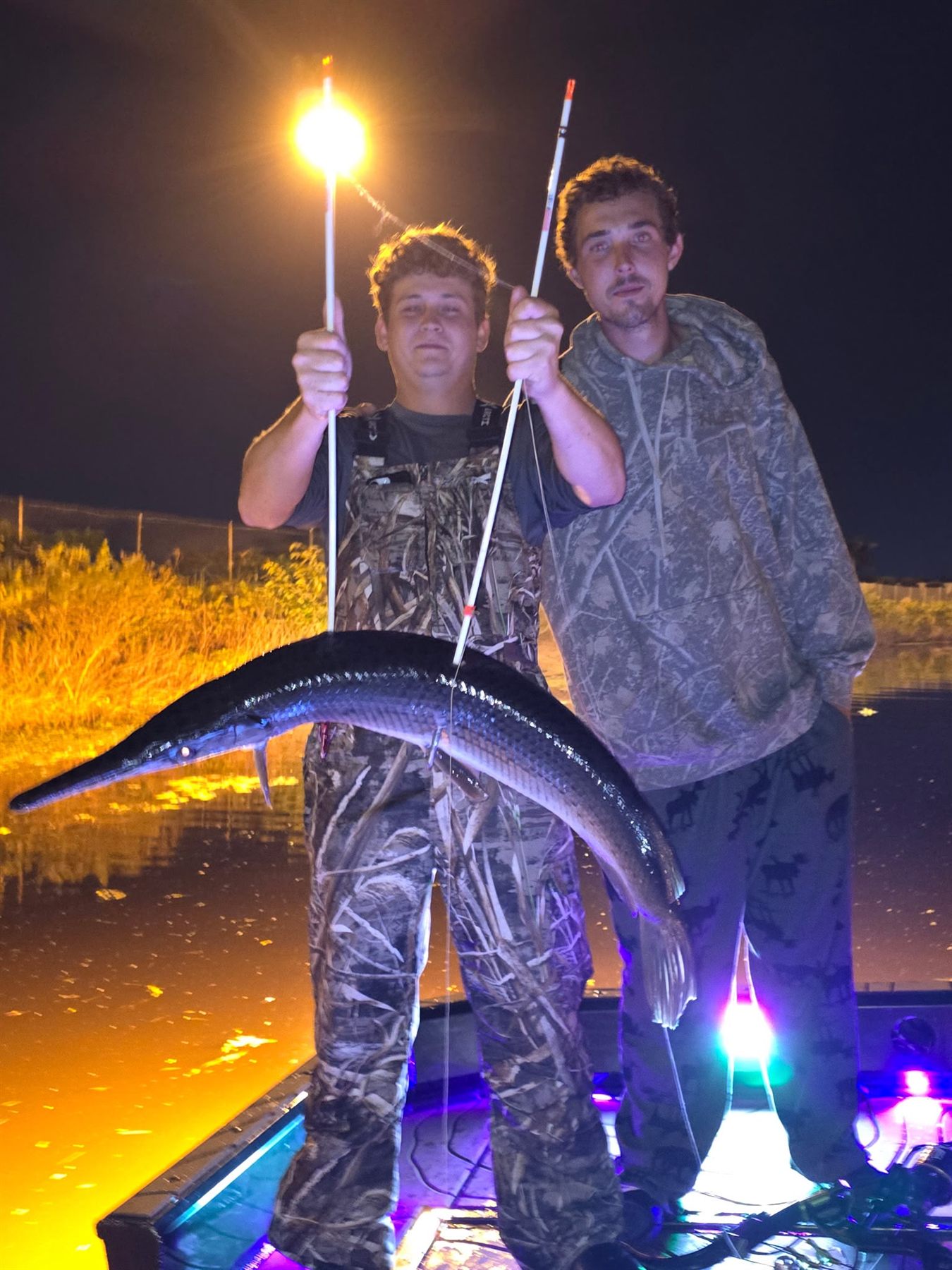 Two guests holding a large gar during a Native Roots night bowfishing trip